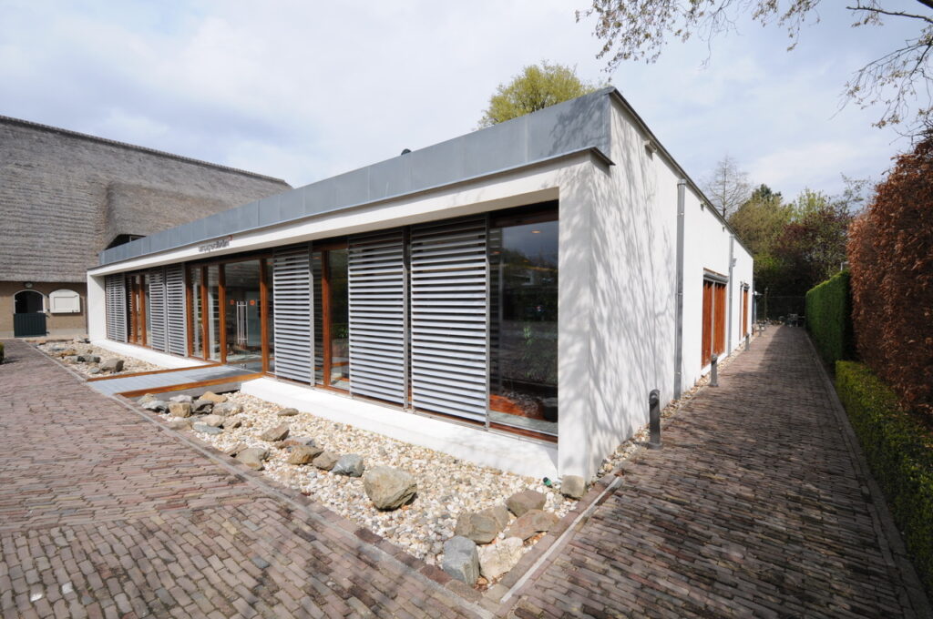 Modern laagbouwgebouw aan de Charloisse Lagedijk met grote ramen en horizontale zonwering, omringd door een bestrate wandelweg en siergrind.